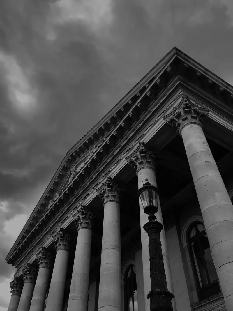 A courthouse pediment and columns under a heavy sky, in black and white