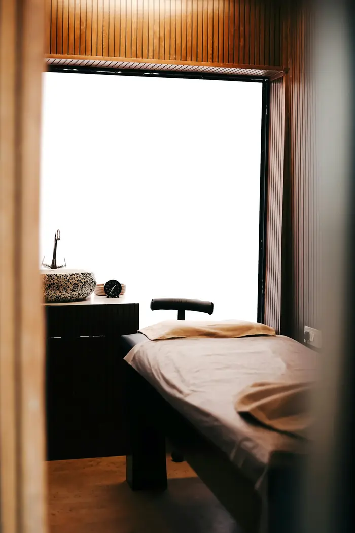 A quiet treatment room with a linen-covered bed beside a tall window