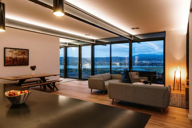 A lounge with low sofas and floor-to-ceiling glass at blue hour